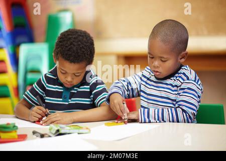 Working together on their creativity. Two preschool african american boys concentrating on thier drawings with thier crayons and shapes. Stock Photo