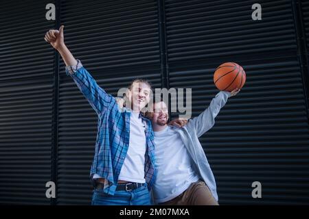 Man with down syndrome playing basketball outdoor with his friend. Concept of friendship and integration people with disability into society. Stock Photo