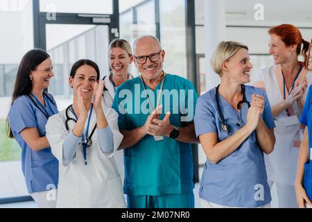 Portrait of happy doctors, nurses and other medical staff clapping, in a hospital. Stock Photo