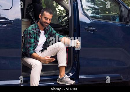man using phone sitting in the door of his camper Stock Photo