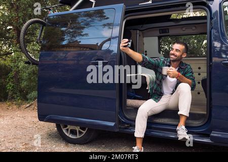 man taking a selfie sitting in the door of his van Stock Photo