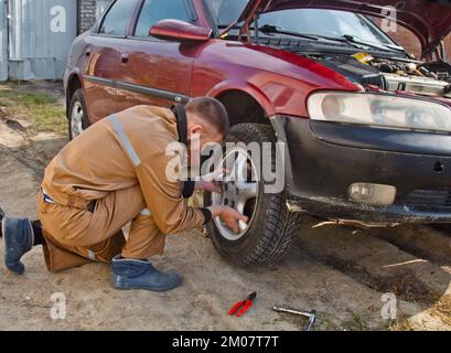 A mechanic removes a car tire. A man working on a machine to remove rubber from a wheel disk Stock Photo