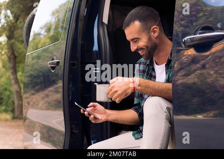 man using his phone sitting in the door of his van Stock Photo