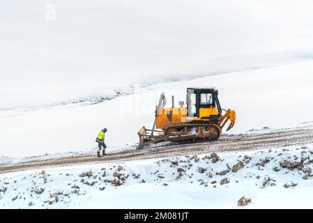 Industrial worker in front of heavy duty bulldozer on road building construction site in winter Stock Photo