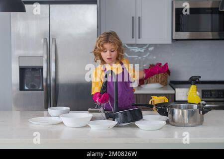 Cleaning at home. Kid wiping dishes in kitchen. Child cleaning and doing housework at home. Cute boy helping with housekeeping in kitchen, cleaning. Stock Photo