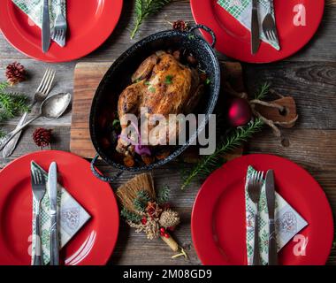 Christmas meal with roasted chicken, vegetable and sauce on rustic and wooden table with red plates, napkins, ornaments and decoration. Flat lay Stock Photo