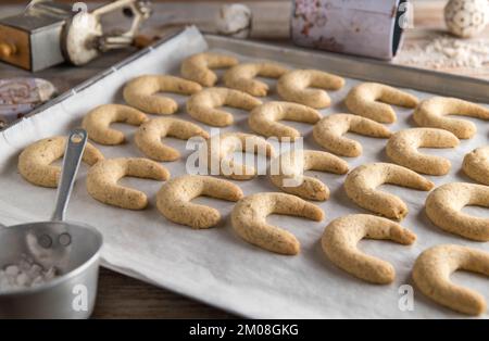 Fresh baked christmas cookies, vanillekipferl or vanilla crescents on a baking sheet with old fashioned kitchen utensils. Stock Photo