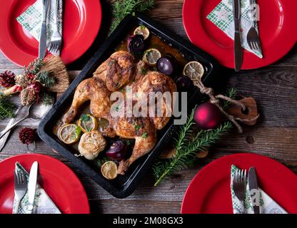 Christmas poultry with fresh roasted flat whole chicken with garlic, lemon and herbs. Served on wooden table with red plates and decoration. Flat lay Stock Photo