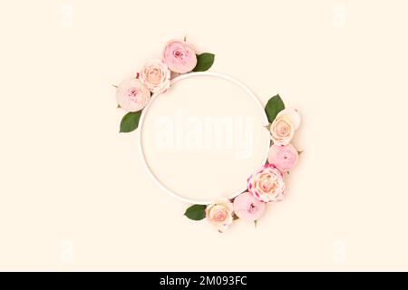 Wreath made of green leaves and pink rose flowers on a beige background. Stock Photo
