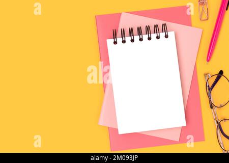Workspace with blank notepad mockup and pink colored stationery on a yellow background. Office supplies. Stock Photo