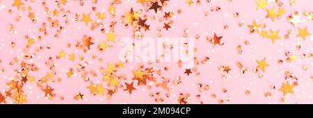 Banner with shiny gold colored stars and crystals confetti on a pink background. Festive texture. Selective focus. Stock Photo