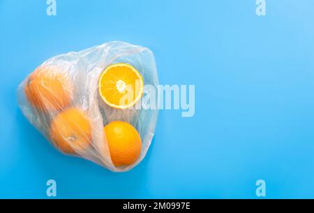 Oranges in plastic bag isolated on blue, flat lay. Stock Photo