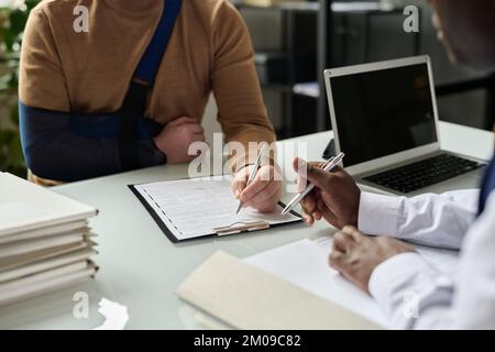 Close up of man filling in medical insurance form, injured hand in sling in background, copy space Stock Photo