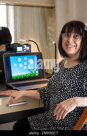 Attractive middle aged woman in front of laptop screen, online teaching concept. Stock Photo