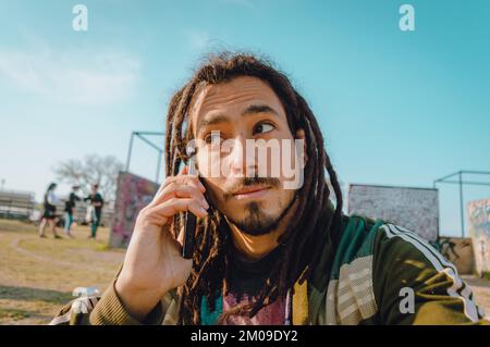 portrait of young caucasian venezuelan man with dreadlocks and beard, talking on the phone and looking to the side, listening carefully and thinking, Stock Photo