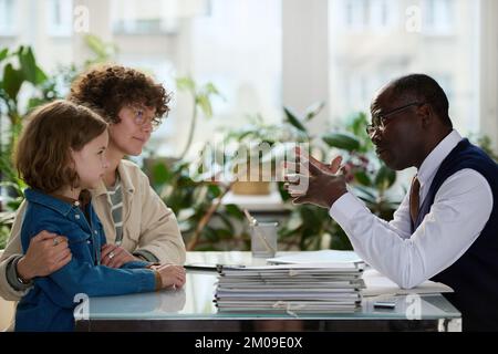 Side view portrait of caring black social worker consulting mother and child in adoption agency office Stock Photo