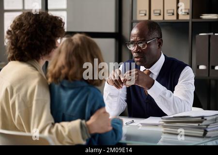 Portrait of caring black man as social worker talking to mother and child in office Stock Photo