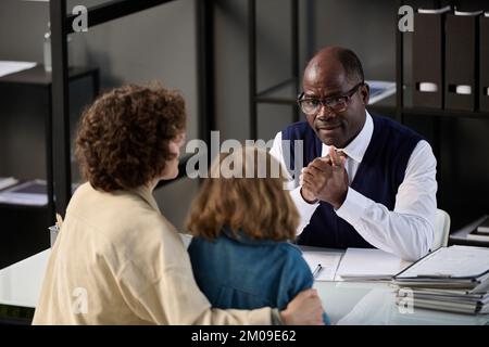 High angle portrait of young mother with child talking to caring black social worker in office Stock Photo