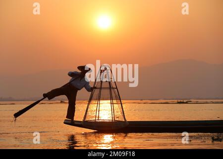 A silhouette of a fisherman near lake catching fish in a traditional way with a handmade net at sunset Stock Photo