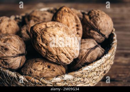 Close-up, whole walnuts in a wicker bowl on a wooden background. Stock Photo