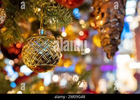 Golden Christmas ball hanging on fir tree against blurred festive lights Stock Photo