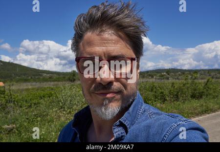 Portrait of mature age, middle age, mid adult man in 50s, happy confident smile, outdoor in strong wind. Stock Photo