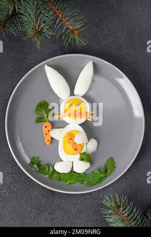 Funny rabbit made from boiled eggs, peeled carrots and arugula on gray plate. Creative food idea for kids, Vertical image Stock Photo