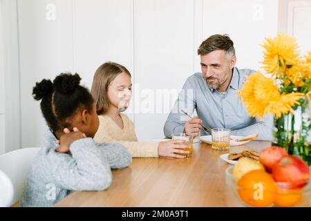Smiling father having breakfast with interracial daughters. Adoption concept. Stock Photo