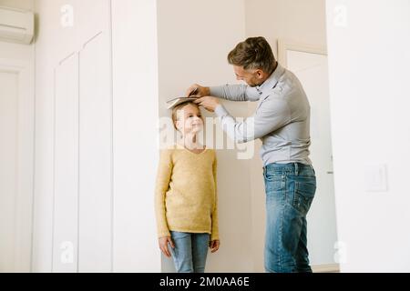 Father measures his little daughter's height by drawing a mark on the wall at home Stock Photo