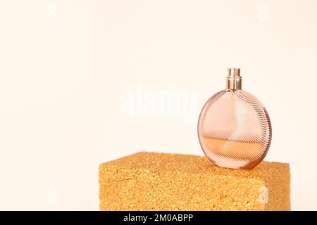 Unbranded round glass perfume bottle on golden podium on ivory background. Eau de toilette. Mockup, copy space Stock Photo