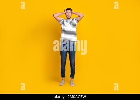 Full length photo of impressed funky guy dressed striped t-shirt arms head isolated yellow color background Stock Photo