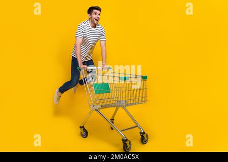 Full length photo of funky impressed man wear white t-shirt jumping high enjoying retail shopping isolated yellow color background Stock Photo