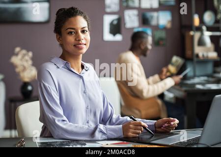 Portrait of smiling graphic designer working on project at office desk Stock Photo