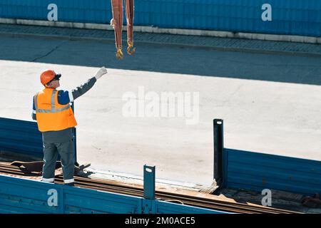Slinger in helmet and vest unloads metal pipes and fittings from truck ...