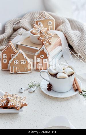 Homemade cute Christmas cookies in shape of houses and cup of warm cocoa with marshmallows. Aesthetics white female Christmas background. Stock Photo