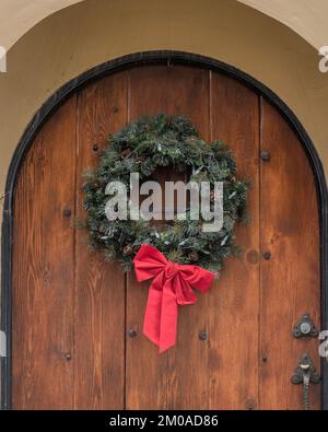 A holiday evergreen Christmas wreath with a red ribbon hangs on a door. Stock Photo
