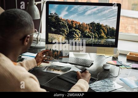Edor looking at reference photo when coloring photo of landscape on screen Stock Photo