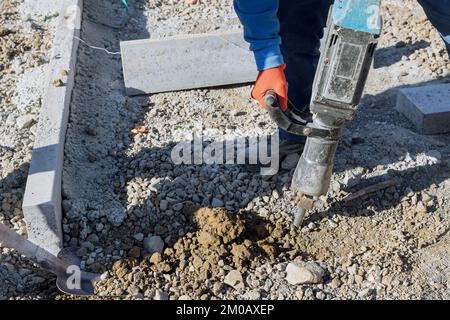 Worker digging and drilling concrete surfaces using jackhammer as part of construction road construction Stock Photo