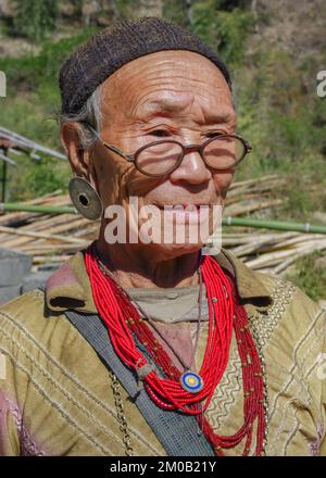 Raga, Arunachal Pradesh, India - 11 20 2013 : Portrait of old Nyishi tribe woman with glasses wearing traditional earrings and red necklaces Stock Photo