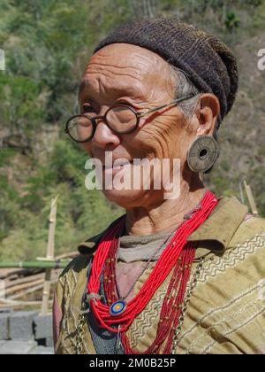 Raga, Arunachal Pradesh, India - 11 20 2013 : Portrait of smiling old Nyishi tribe woman with glasses wearing traditional earrings and red necklaces Stock Photo