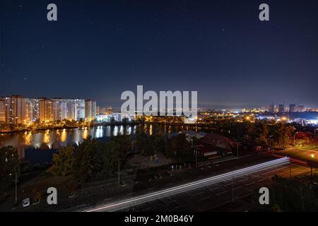 Night cityscape of the big city under starry sky. Awesome bright, multi colored light at curfew on empty streets. Apartment buildings in bedroom town Stock Photo