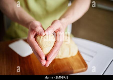 Working at home kitchen concept, homemade baking. Man chef baker in green apron holding dough ball in hands folded in heart shape. High quality photo Stock Photo