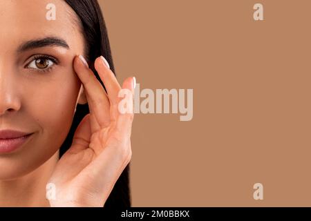Half face of attractive brunette woman touching under eye skin Stock Photo