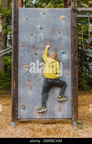 Boy At The Climbing Wall Without A Helmet, Danger At The Climbing Wall. Little Boy Climbing A Rock Wall Indoor Stock Photo