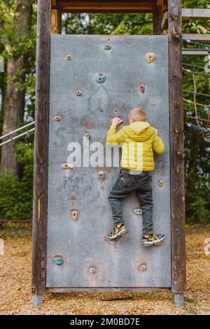 Boy At The Climbing Wall Without A Helmet, Danger At The Climbing Wall. Little Boy Climbing A Rock Wall Indoor Stock Photo