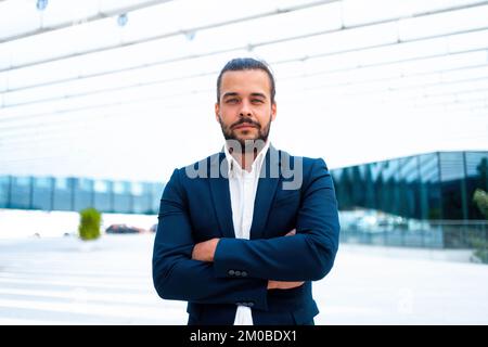 Confidence successful businessman or worker in suit with beard standing in front of office glass building arm crossed. Hispanic handsome business man looking at camera. Portrait shoot. Front view Stock Photo