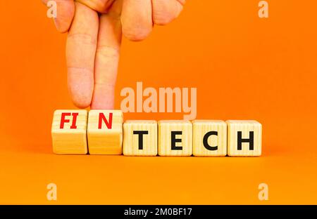 Tech or fintech symbol. Concept word Tech and Fintech on wooden cubes. Businessman hand. Beautiful orange table orange background. Business and tech o Stock Photo