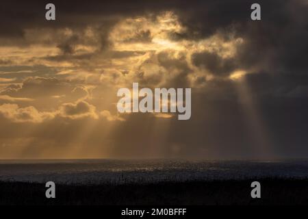 Beautiful cloudscape over the North Sea on the East Coast of Yorkshire. Warm yellow sun rays penetrate the clouds and shine on the dark water giving a Stock Photo