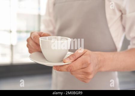 Your coffee, please. Cropped image of a man holding a cup of good coffee against the background of a window. With space to copy. High quality photo Stock Photo