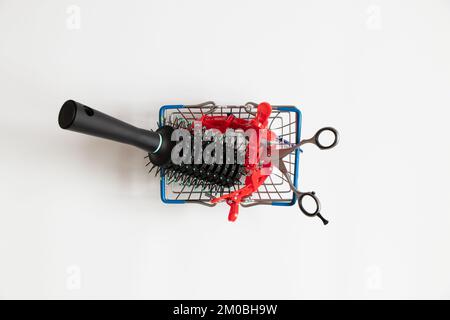 Scissors and a hair clip and a comb lie in a supermarket basket on a white background, a hairdresser's set, business and services Stock Photo